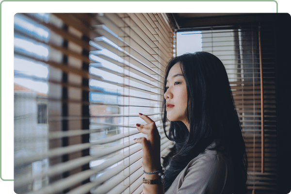 lady looking out of a window between blinds
