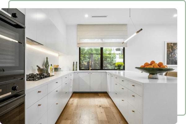 a clean modern white kitchen with wooden floors and black appliances and a black window frame.